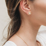 Close-up side view of a woman’s ear wearing a gold star stud earring, with her hair tucked behind the ear.