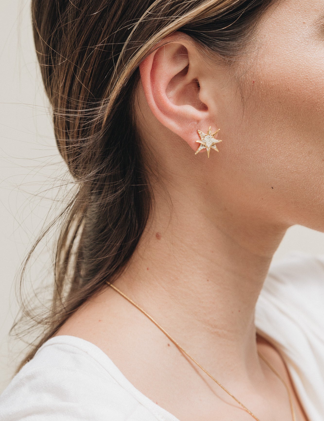 Close-up side view of a woman’s ear wearing a gold star stud earring, with her hair tucked behind the ear.